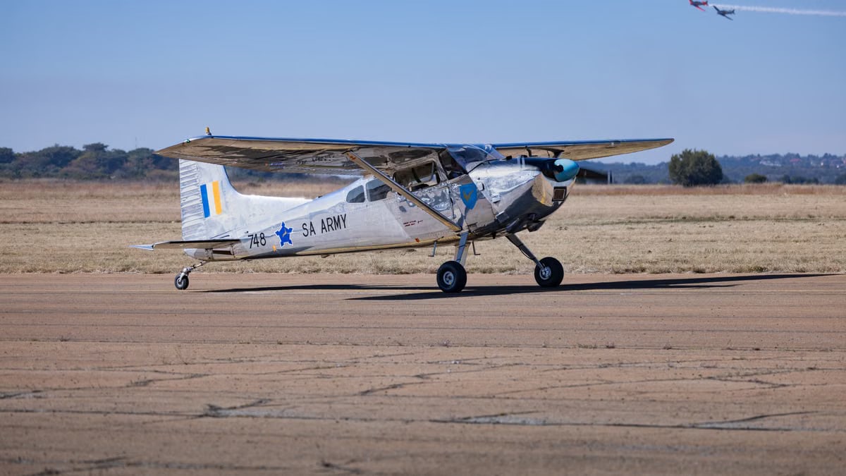 A classic SA Army airplane captured on the runway with a formation of jets in the sky.